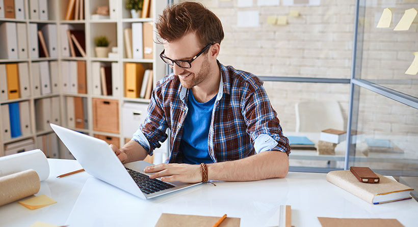 Ein Mann sitzt an einem Laptop arbeitend am Schreibtisch. Repräsentiert Arbeit im Homeoffice.